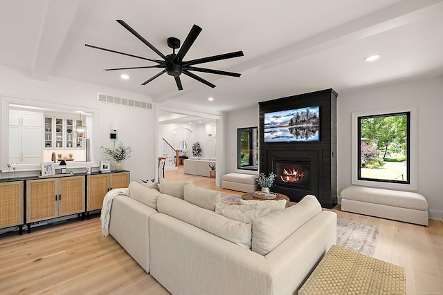 living room featuring a large fireplace, light wood-type flooring, beamed ceiling, and ceiling fan