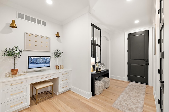 office with light hardwood / wood-style flooring, crown molding, and built in desk