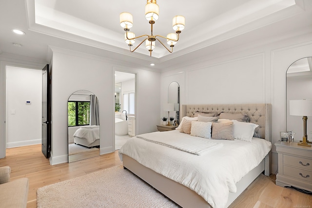 bedroom featuring light wood-type flooring, ensuite bath, a notable chandelier, and a raised ceiling