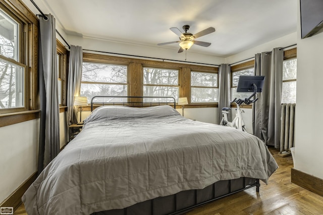 bedroom featuring ceiling fan, wood-type flooring, multiple windows, and radiator heating unit