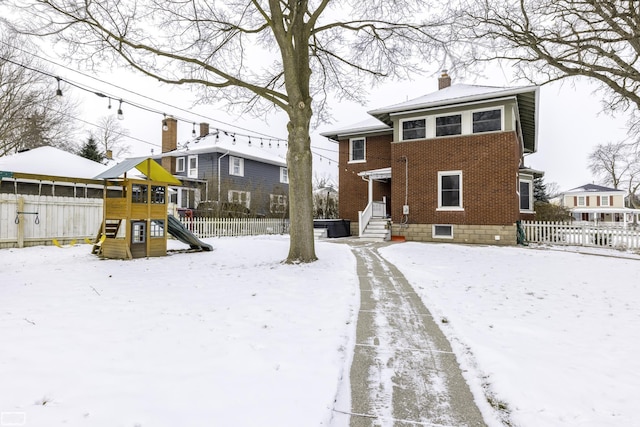 snow covered back of property with a playground