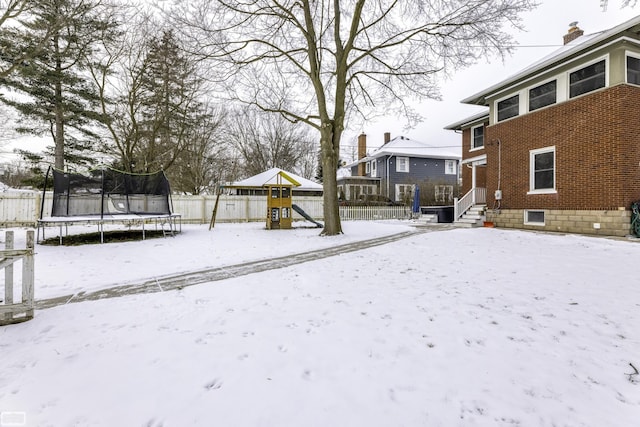 yard layered in snow with a playground and a trampoline