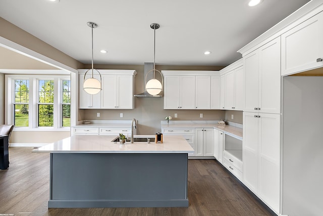 kitchen featuring pendant lighting, white cabinetry, wall chimney exhaust hood, and a kitchen island with sink