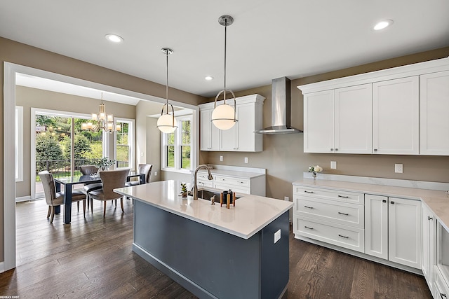 kitchen with white cabinetry, wall chimney exhaust hood, decorative light fixtures, and an island with sink