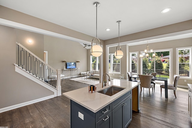 kitchen featuring dark wood-type flooring, an island with sink, decorative light fixtures, and sink