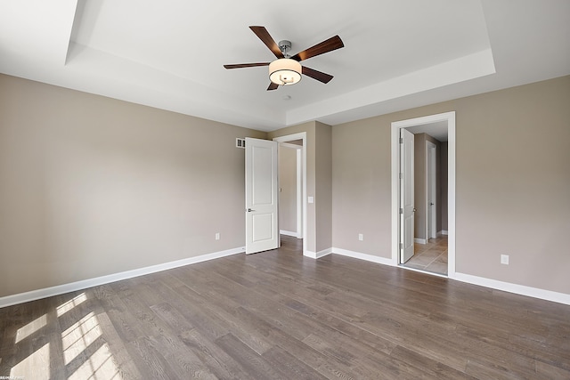 unfurnished bedroom with a raised ceiling, wood-type flooring, ceiling fan, and ensuite bath