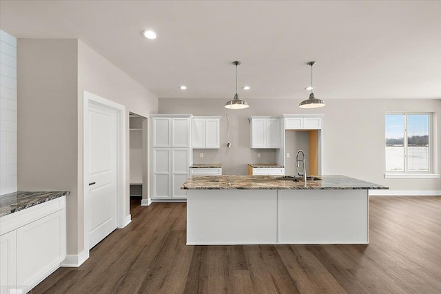 kitchen featuring dark hardwood / wood-style floors, decorative light fixtures, white cabinetry, sink, and dark stone countertops