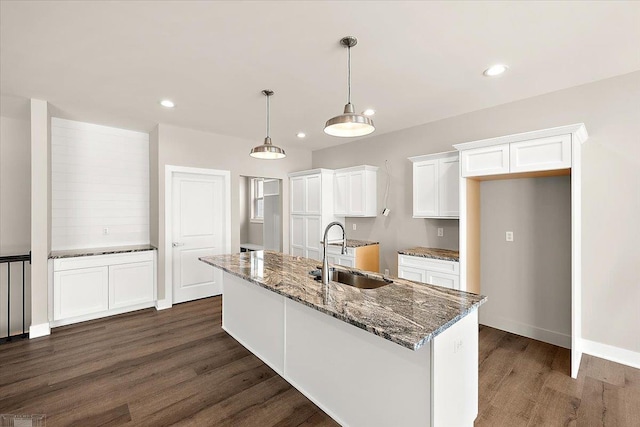 kitchen featuring pendant lighting, sink, white cabinetry, dark stone countertops, and a center island with sink