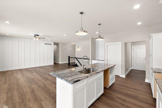 kitchen featuring sink, white cabinetry, a kitchen island with sink, hanging light fixtures, and dark stone countertops