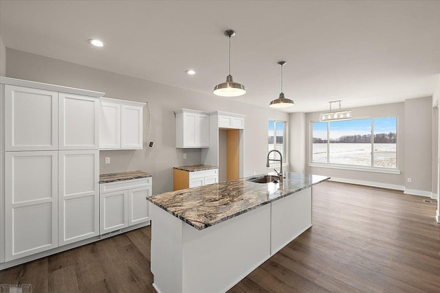 kitchen with white cabinetry, sink, dark stone countertops, and a center island with sink