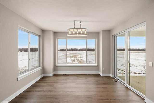 unfurnished dining area featuring wood-type flooring, a healthy amount of sunlight, and an inviting chandelier