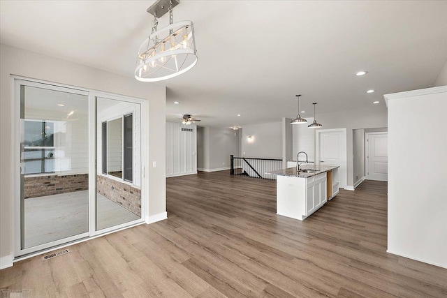 kitchen with decorative light fixtures, white cabinetry, wood-type flooring, sink, and a center island with sink