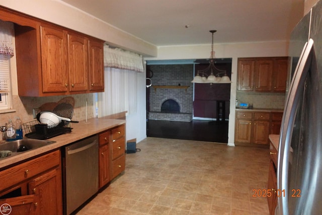 kitchen featuring sink, stainless steel appliances, tasteful backsplash, a brick fireplace, and decorative light fixtures