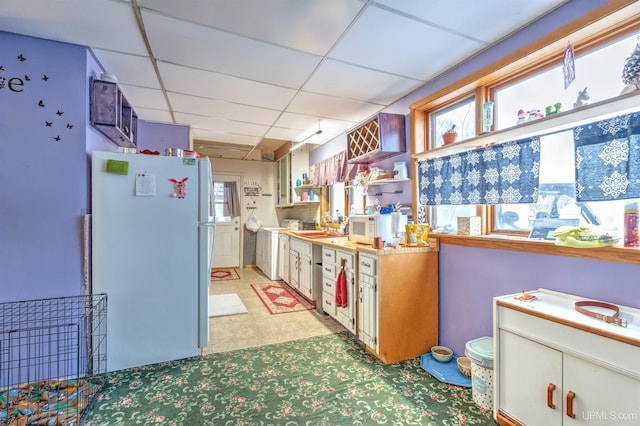 kitchen featuring a drop ceiling, washer / clothes dryer, a healthy amount of sunlight, and white fridge