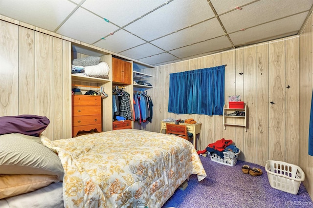 bedroom with wood walls, carpet, a drop ceiling, and a closet