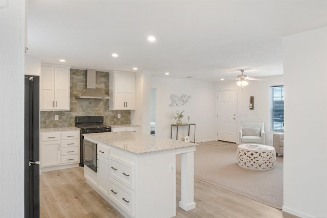 kitchen with white cabinetry, gas range, a kitchen island, and wall chimney range hood