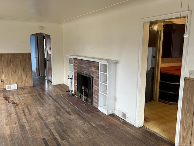 unfurnished living room with dark hardwood / wood-style flooring, a fireplace, and wood walls