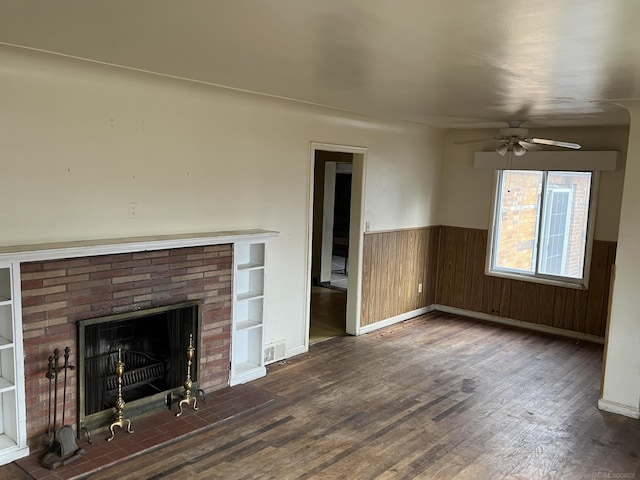 unfurnished living room featuring built in features, wooden walls, a fireplace, dark hardwood / wood-style flooring, and ceiling fan