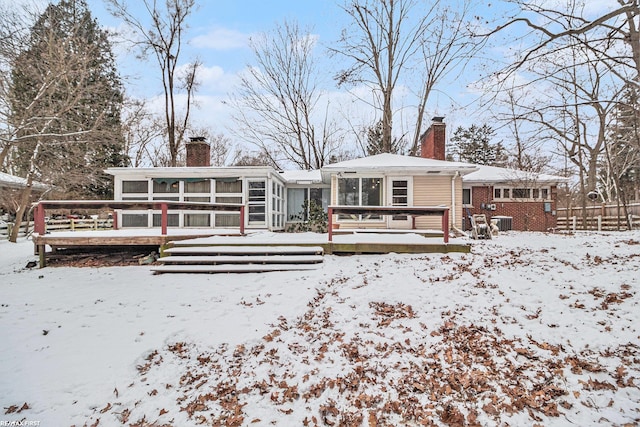 snow covered back of property with a deck and a sunroom