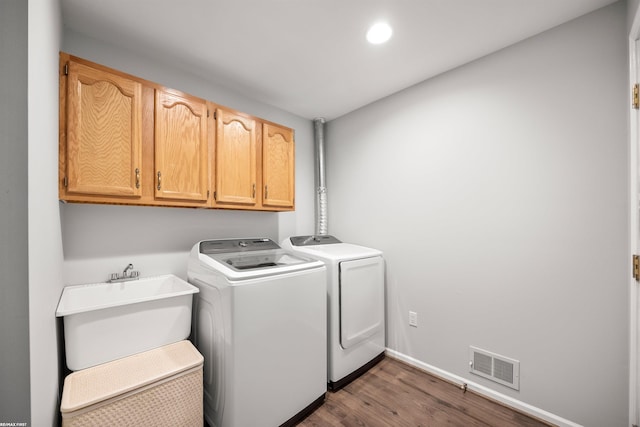 clothes washing area with sink, wood-type flooring, cabinets, and washing machine and clothes dryer