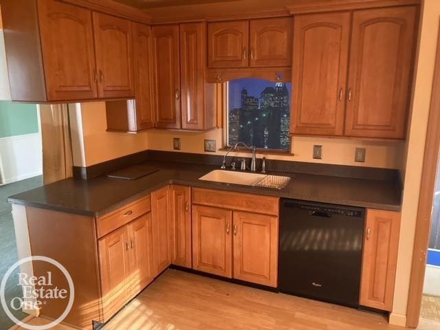 kitchen with black dishwasher, brown cabinets, dark countertops, light wood-style floors, and a sink