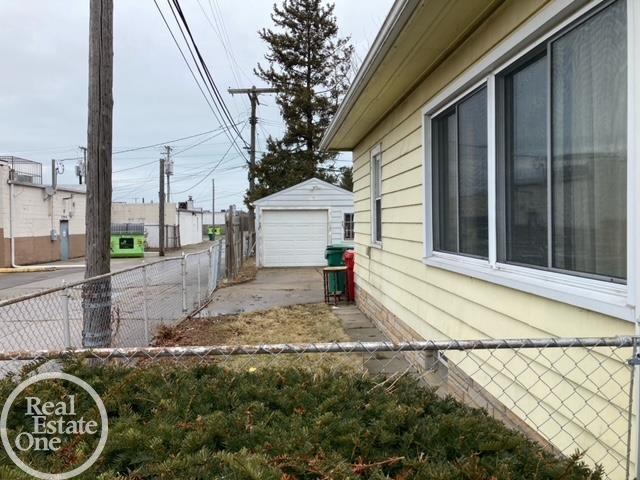 view of side of home featuring driveway, a detached garage, fence, and an outbuilding