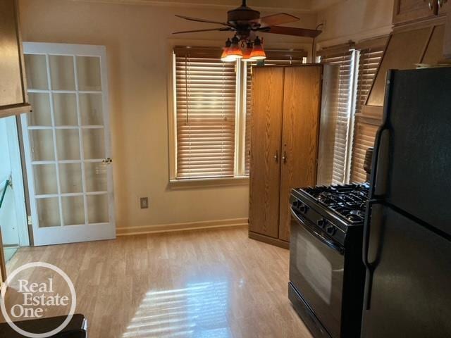 kitchen with light wood-style flooring, black gas range oven, a ceiling fan, freestanding refrigerator, and baseboards