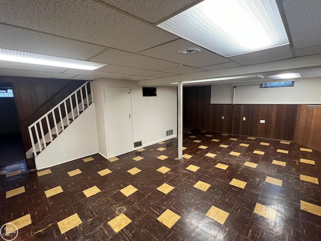 basement featuring a paneled ceiling and wooden walls