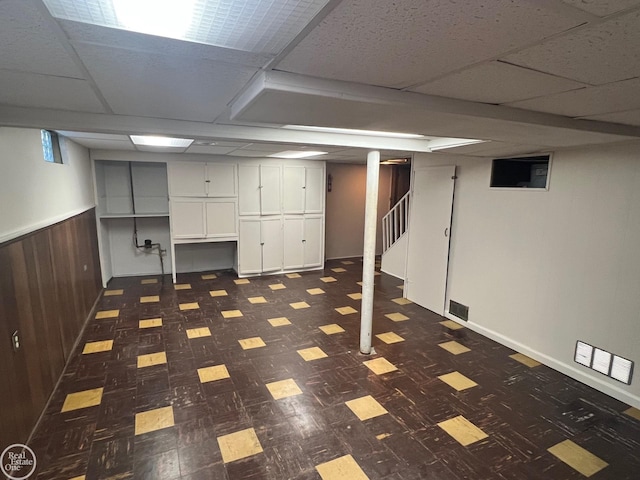 basement with a paneled ceiling and wood walls