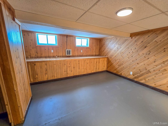 basement with a drop ceiling and wood walls