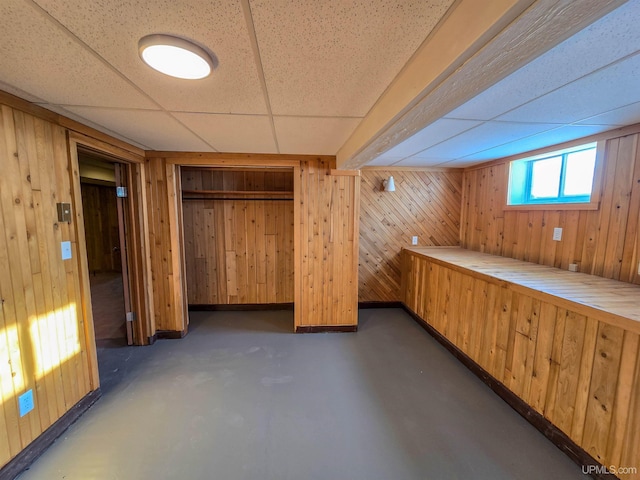 basement featuring a drop ceiling and wood walls