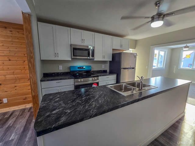 kitchen featuring sink, wood walls, an island with sink, stainless steel appliances, and white cabinets