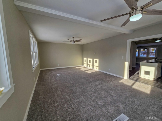 unfurnished living room with beamed ceiling, dark colored carpet, sink, and ceiling fan