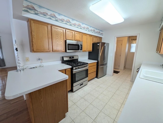 kitchen with a kitchen bar, sink, a textured ceiling, kitchen peninsula, and stainless steel appliances