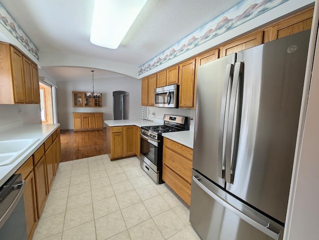 kitchen with sink, appliances with stainless steel finishes, hanging light fixtures, kitchen peninsula, and a chandelier