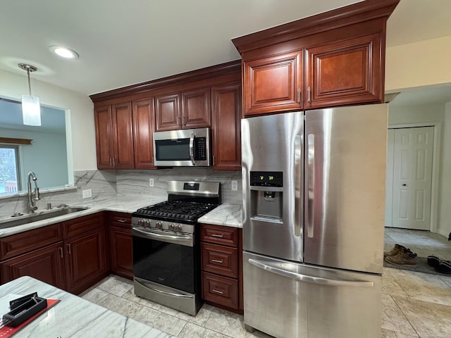 kitchen with sink, decorative light fixtures, light stone countertops, and appliances with stainless steel finishes