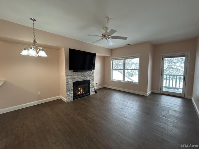 unfurnished living room with a stone fireplace, ceiling fan with notable chandelier, and dark hardwood / wood-style flooring