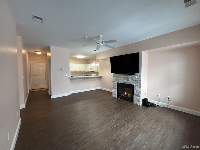 unfurnished living room featuring a stone fireplace, dark wood-type flooring, and ceiling fan