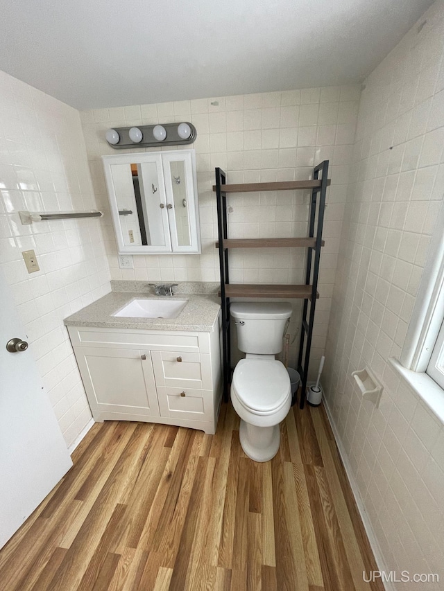 bathroom featuring wood-type flooring, tile walls, vanity, and toilet