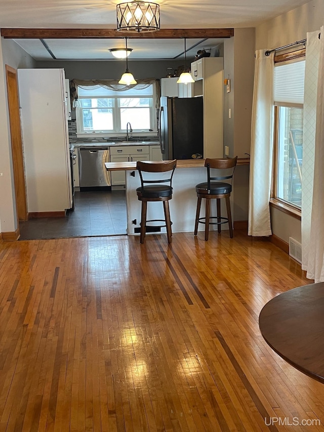 kitchen with decorative light fixtures, sink, a kitchen bar, fridge, and stainless steel dishwasher