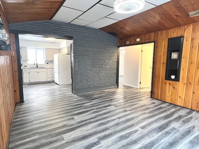 unfurnished living room with lofted ceiling, sink, and wood walls