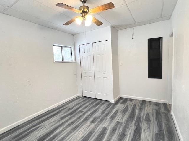 unfurnished bedroom with dark wood-type flooring, a paneled ceiling, ceiling fan, and a closet