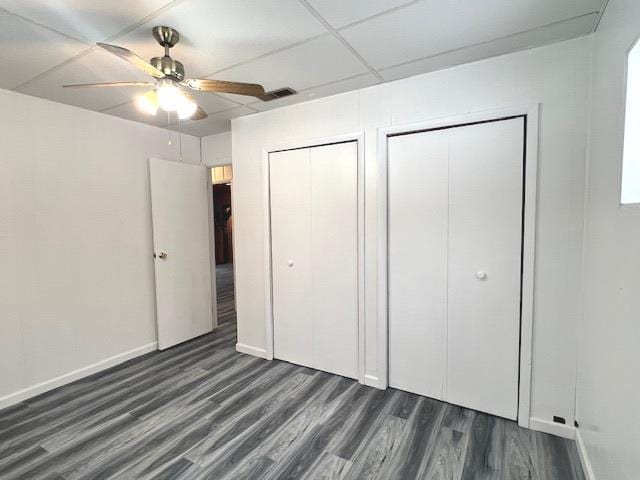 unfurnished bedroom featuring multiple closets, ceiling fan, dark hardwood / wood-style floors, and a paneled ceiling