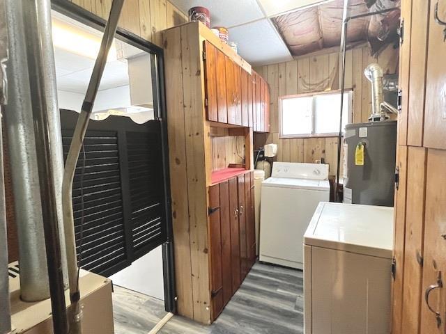 laundry area featuring hardwood / wood-style flooring, gas water heater, washing machine and dryer, and wooden walls