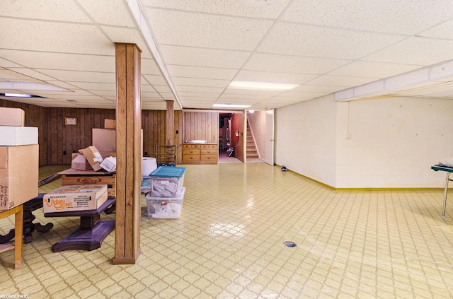 basement featuring a drop ceiling and wood walls