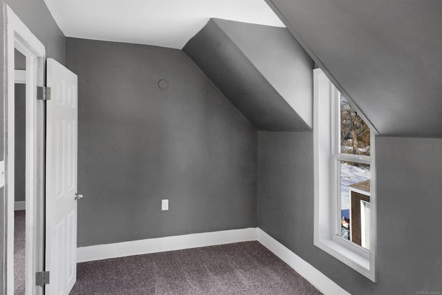 additional living space featuring lofted ceiling, dark carpet, and plenty of natural light