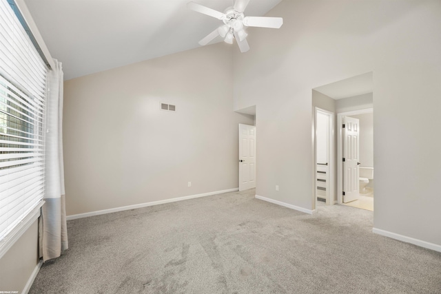 unfurnished bedroom with ceiling fan, high vaulted ceiling, ensuite bathroom, a fireplace, and light colored carpet