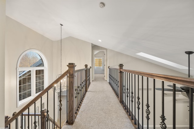 hallway with light colored carpet, a healthy amount of sunlight, lofted ceiling with skylight, and a notable chandelier