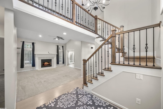 staircase with a tile fireplace, ceiling fan with notable chandelier, carpet, and a high ceiling