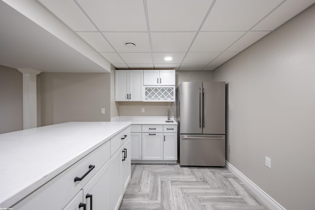 kitchen featuring stainless steel refrigerator, white cabinetry, sink, light parquet flooring, and a drop ceiling